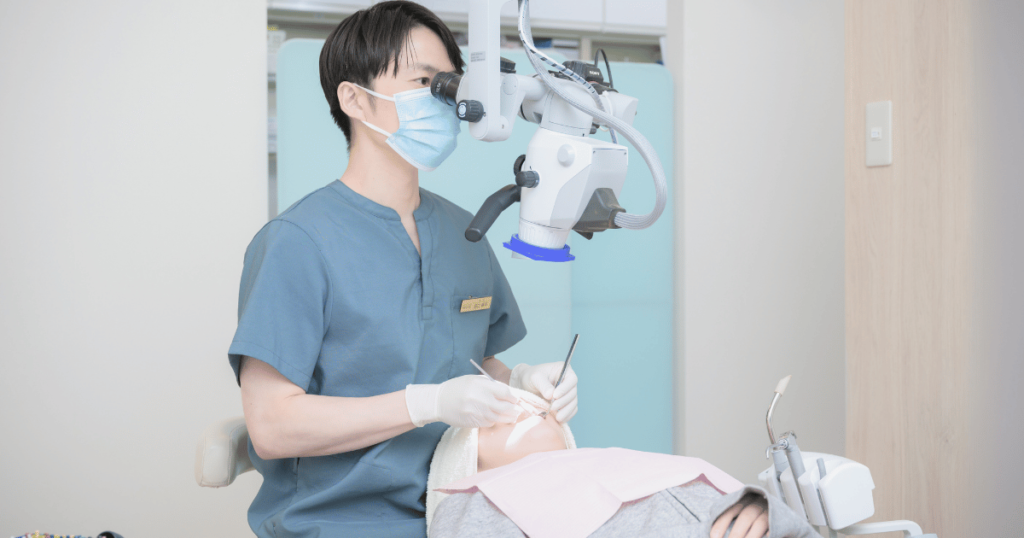 マイクロスコープを使用して歯のブリッジ治療を行う歯科専門医の診療風景。寿命の長い補綴治療を提案するシーン